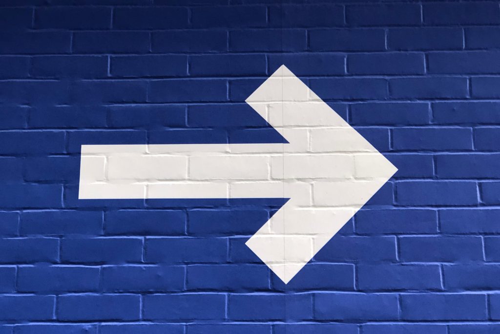 Photo of big white arrow on a blue brick wall by Nick Fewings on Unsplash